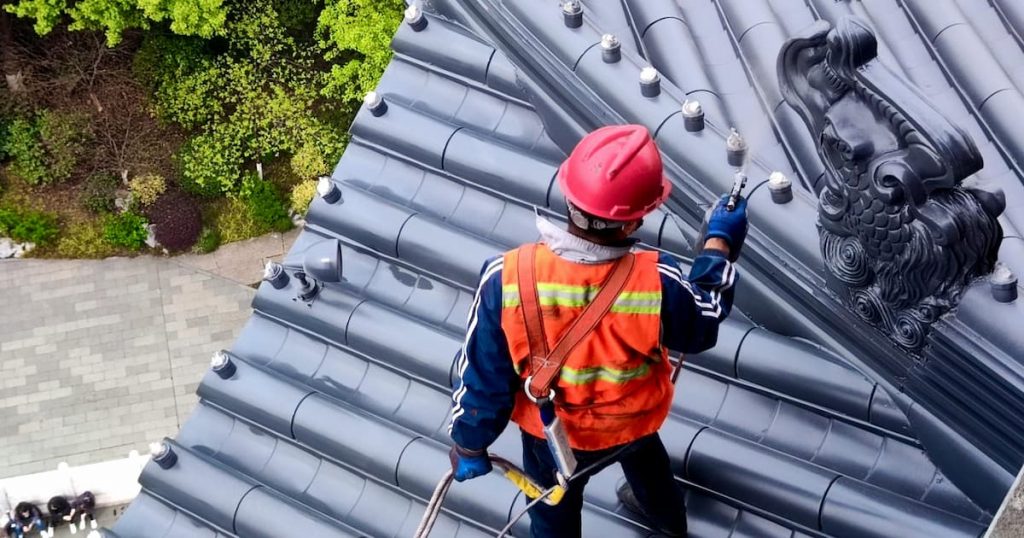 man safely working on a roof weaing safety harnesses hi vis and hard hat